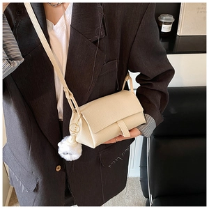 Detail of beige litchi grain leather crossbody bag with cute plush ball pendant
