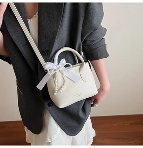 Detail of cream crossbody bucket bag with pearl chain and silk bow decoration