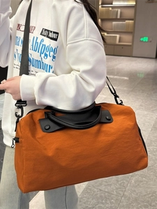 Large orange travel duffel bag with black straps for gym and short trips, shown by model