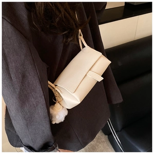 Detail view of beige crossbody bag with textured leather and white pompom charm