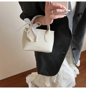 Detail of cream white leather bucket bag with pearl bow and silk ribbon decoration