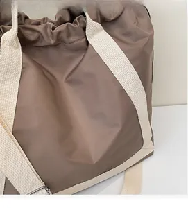 Detail of soft brown nylon fabric and white canvas straps on a drawstring tote bag