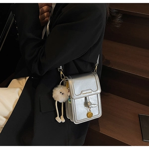 Detail of silver textured mini crossbody bag with a plush charm and fashion text
