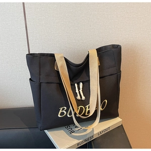 Detail of black canvas tote bag featuring gold BUDELLO embroidery and woven straps