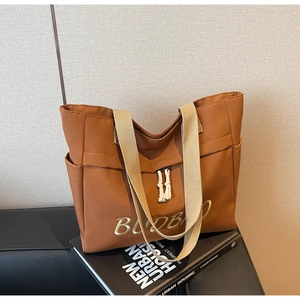 Detailed view of brown canvas tote bag with woven handles and white cotton tassel fringe