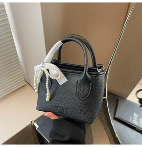 Detail of black litchi leather bucket bag featuring a pearl bow and logo imprint
