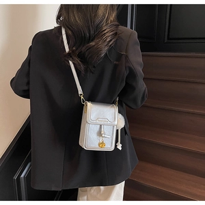 Silver metallic crossbody phone bag with knot tassel and plush ball detail on black suit