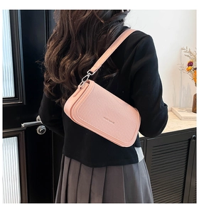 Detail of light pink crossbody bag with woven texture and adjustable strap on a shoulder