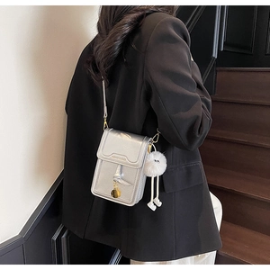Detail of silver metallic crossbody phone bag with plush charm on a model in dark setting