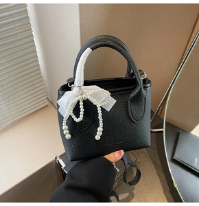 Close-up of black lychee texture leather bucket bag with bow and pearl charms