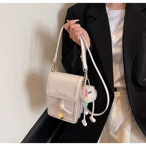 Detail of cream square crossbody phone bag with FASHION & BAGS logo and plush charm