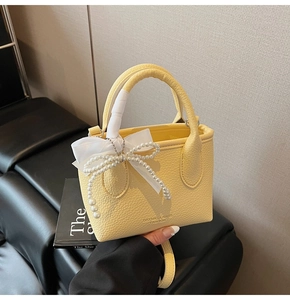 Detail of yellow lychee grain bucket bag featuring pearl and white silk bow charms
