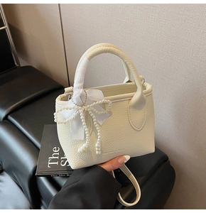 Detail of off-white lychee leather bucket bag with silk ribbon handle and pearl bow charm