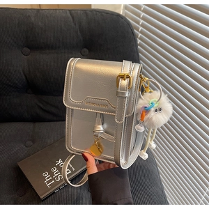 Detail of silver metallic mini square bag with golden lock and fuzzy charm on black sofa