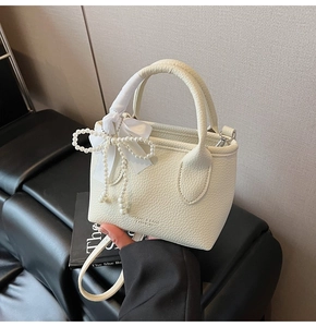 Close-up of cream leather bucket bag with elegant pearl and silk bow charm detail