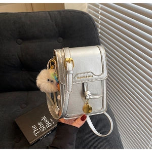 Detailed shot of silver PU leather crossbody bag with golden buckle and plush ball charm