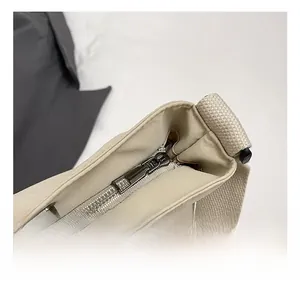 Détail du sac cabas en toile beige montrant la fermeture éclair et le bouton pression métal