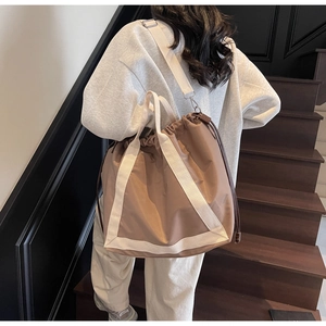 Detail of brown nylon tote bag showing drawstring closure and wide fabric shoulder strap