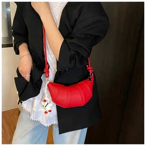 Close-up of a red croissant bag in lychee leather with a cute duck charm on model