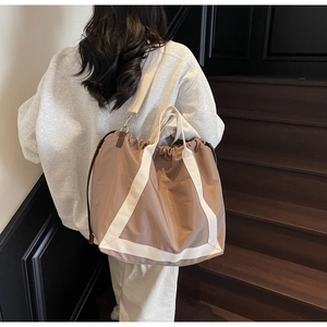Khaki nylon tote bag with white webbing straps and drawstring detail shown on a model