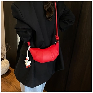 Detail of red crescent leather bag with duck charm styled on a black blazer