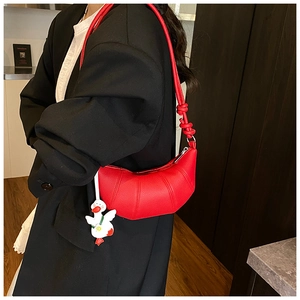 Detail of red crescent leather bag with decorative knot strap and duck pendant charm