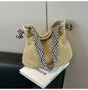 Détail d'un sac cabas en paille avec bandoulières rayées noir et blanc et décor de nœuds
