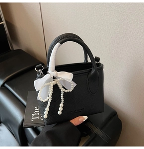 Detail of black lychee grain bucket bag with white ribbon and pearl bow pendant