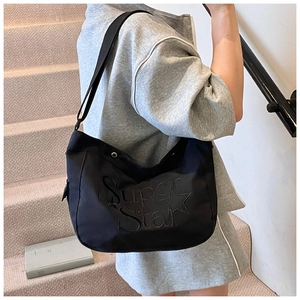 Détail du sac cabas noir avec broderie Super Star porté à l'épaule par le mannequin