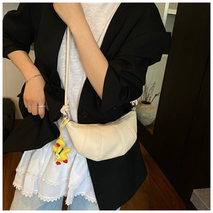 Detail of a beige croissant crossbody bag featuring quilted folds and a yellow duck charm