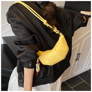 Close-up of yellow leather croissant bag with pebble texture and swan pendant charm