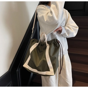 Detail of army green nylon tote bag with drawstring closure and white canvas strap detail