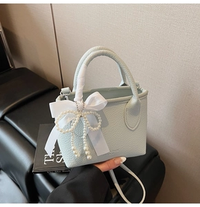 Detail of light blue lychee pattern leather bag with silk bow and pearl charm