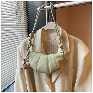 Detail of avocado green pebbled leather croissant bag with cute duck charm on blazer