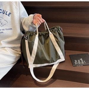 Detail of olive green nylon tote bag with drawstring texture and canvas straps