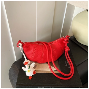 Close-up of red lychee grain leather croissant bag with cute duck charm and knot strap detail