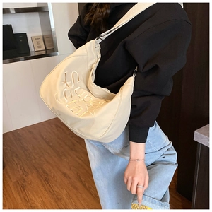 Détail d'un sac demi-lune beige avec broderie Super Star porté par un mannequin