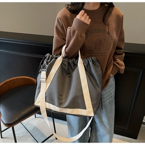 Detail of dark grey nylon tote bag with drawstring closure and cream webbing handles
