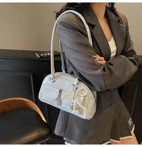 Detail of light gray Boston bag with pearl bow pendant and heart charm on shoulder strap