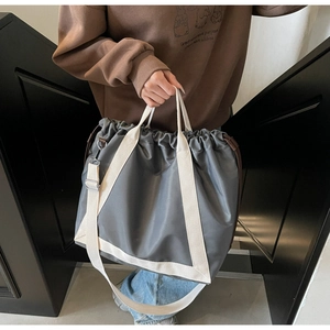 Detail of grey nylon drawstring tote bag with off-white canvas shoulder straps on stairs