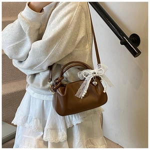 Detalle de un bolso cubo plisado marrón con lazo de encaje blanco y perlas