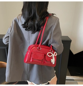 Detail of red patent leather shoulder bag featuring double pockets and pearl bow charm