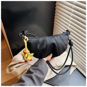 Detail of black litchi grain croissant bag with a cute yellow duck charm and leather strap