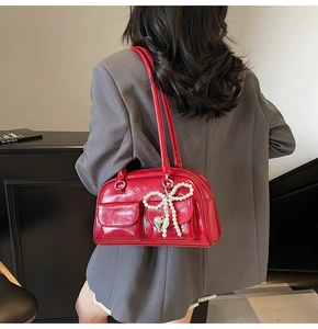 Detail of red glossy shoulder bag with pearl bow charms worn by model from behind