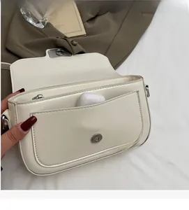 Detail view of the front pocket of a cream PU leather crossbody bag with an earbud case inside