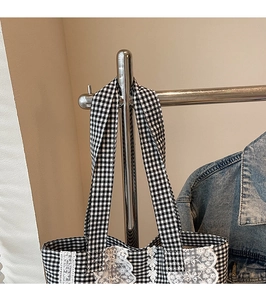 Close-up of black and white checkered tote bag with delicate white lace trim detail