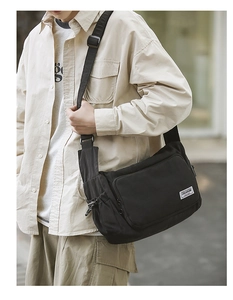 Detail of black nylon messenger bag with front zip pocket and side drawstring pocket