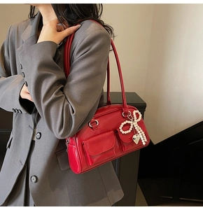 Close-up of red glossy patent leather underarm bag with pearl bow and dual flap pockets