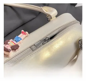 Macro view of cream white leather bag showing silver metal zipper and cute doll charm