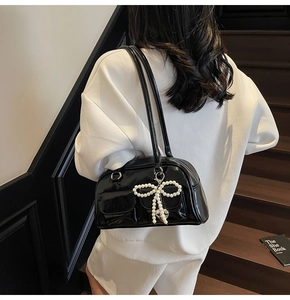 Detail of black patent leather underarm bag with white pearl bow and heart charm on stairs